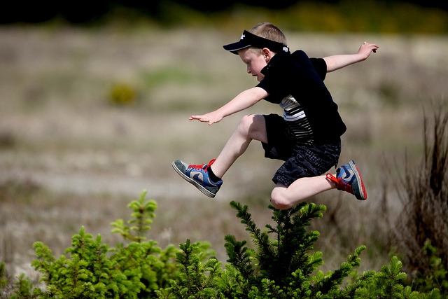 child jumping over hedge